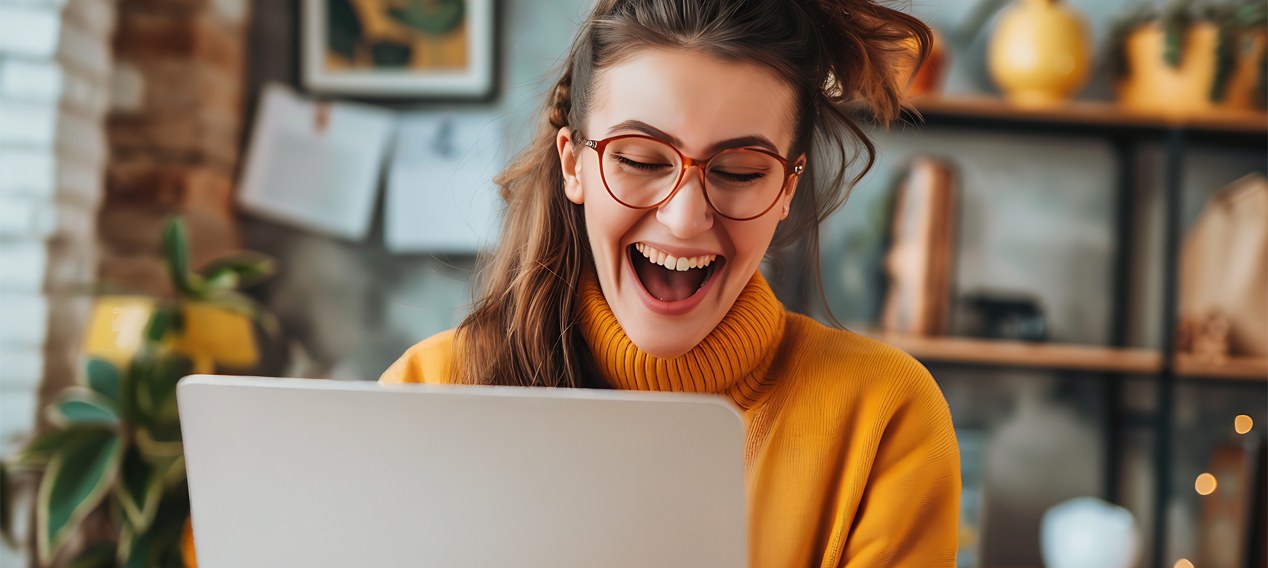 Junge Frau sitzt voller Freude zu Hause vor dem Laptop